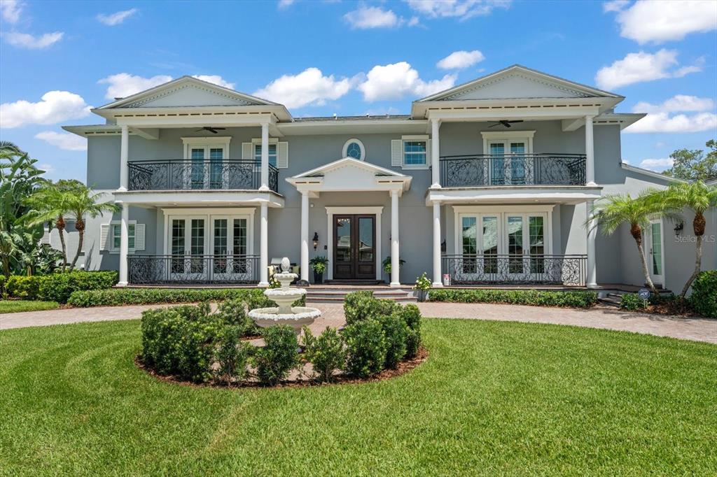 A two-story gray house with a circular driveway, a fountain, and two upper-level balconies — 155 WILLADEL DRIVE, BELLEAIR, FL