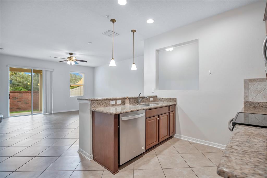 A kitchen with granite countertops and wood cabinets overlooks an open-concept living area with tile — 196 WINDFLOWER WAY, OVIEDO, FL