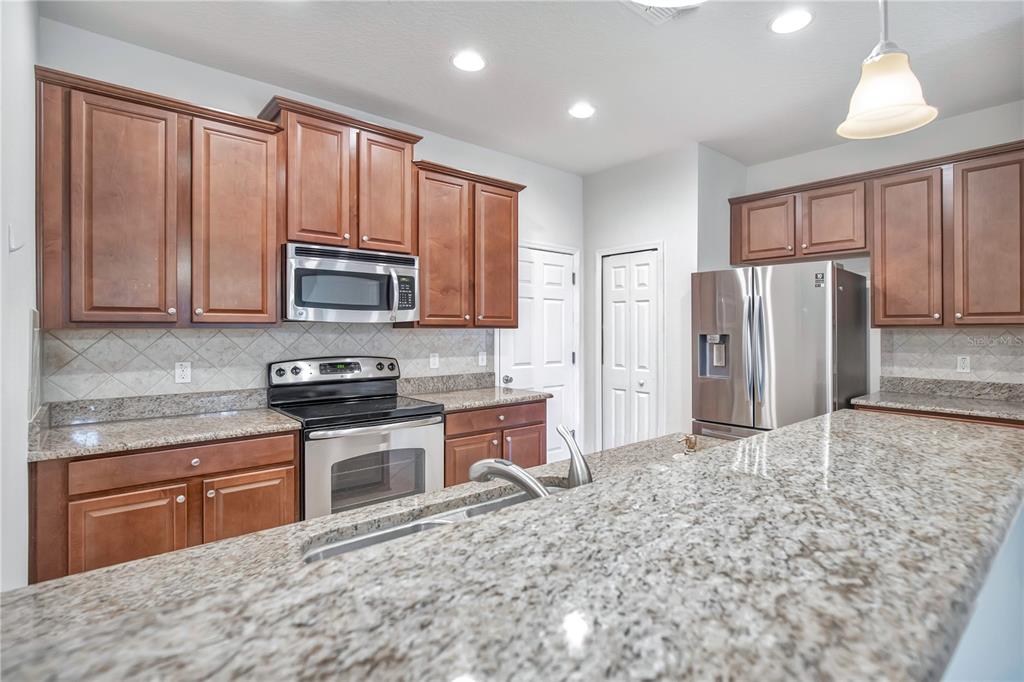 A kitchen features wood cabinets, granite countertops, stainless steel appliances, and a central island — 196 WINDFLOWER WAY, OVIEDO, FL