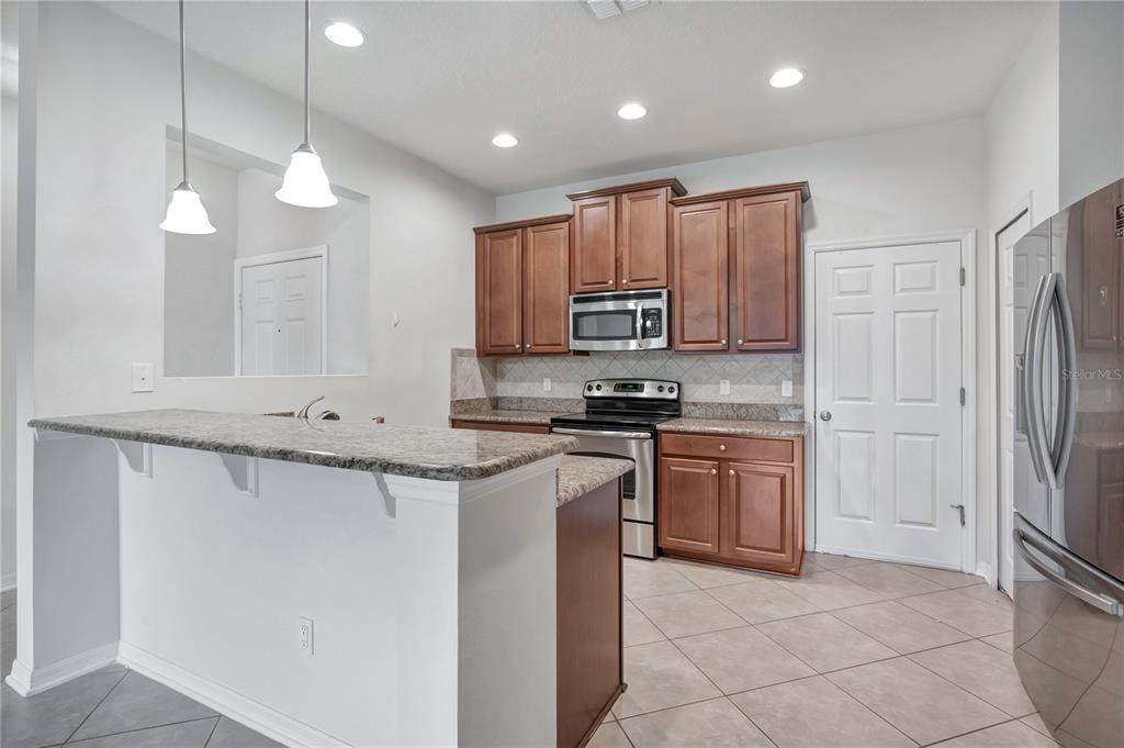 A kitchen features wood cabinets, granite countertops, stainless steel appliances, and a breakfast bar — 196 WINDFLOWER WAY, OVIEDO, FL