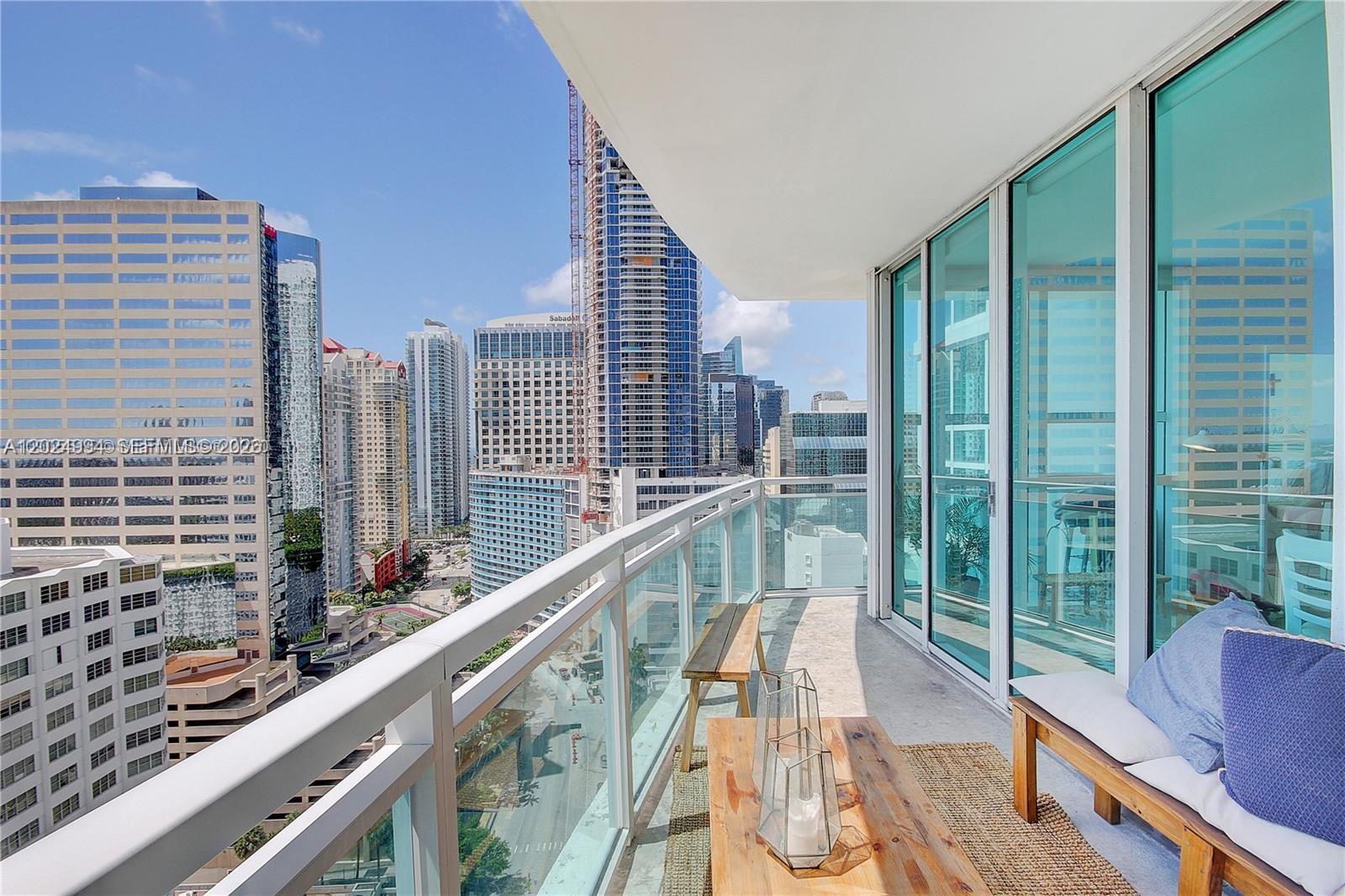 A high-rise balcony features a wooden bench, a coffee table, and views of city skyscrapers — 950 Brickell Bay Dr # 1911, Miami FL 33131, MIAMI, FL
