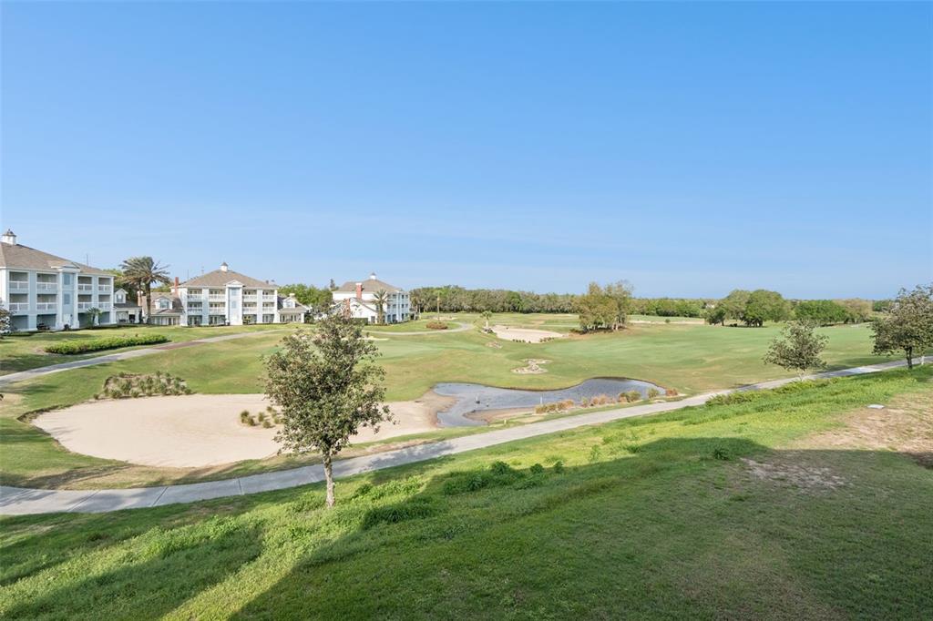 A view of a golf course with a pond, sand traps, and nearby apartment buildings — 7655 HERITAGE CROSSING WAY UNIT 201, REUNION, FL