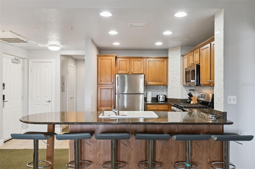 A kitchen with wood cabinets, stainless steel appliances, and a granite-topped island with bar stools — 7655 HERITAGE CROSSING WAY UNIT 201, REUNION, FL