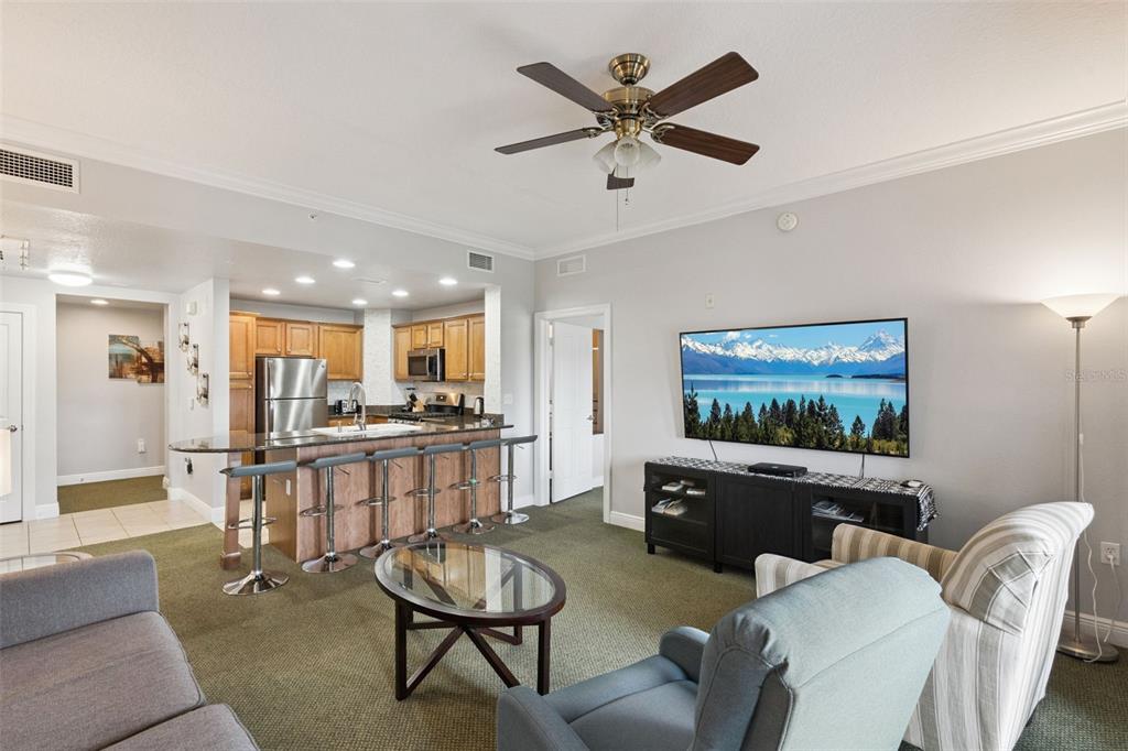 A living room with a kitchen island, bar stools, and a wall-mounted television — 7655 HERITAGE CROSSING WAY UNIT 201, REUNION, FL