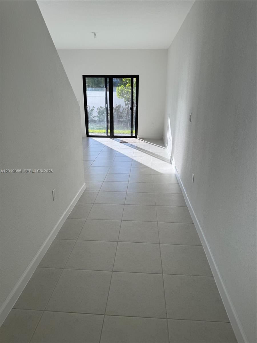 A hallway with light-colored tile flooring leads toward a glass sliding door — 4957 Oakmont Dr # 5838, Dania Beach FL 33312, DANIA BEACH, FL