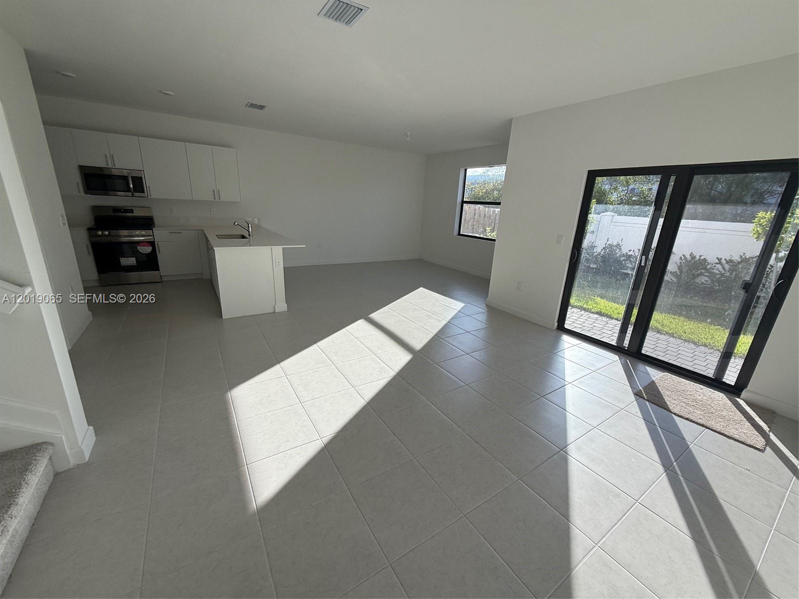 An open-concept kitchen and living area features white cabinetry, tile flooring, and sliding glass doors — 4957 Oakmont Dr # 5838, Dania Beach FL 33312, DANIA BEACH, FL