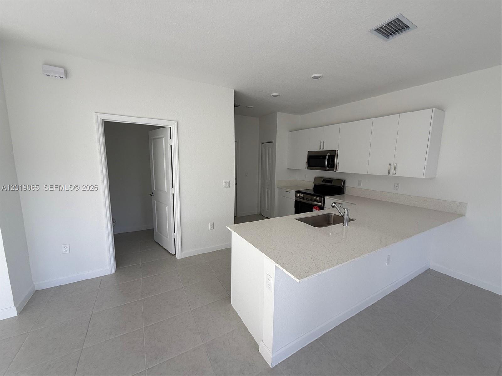 A kitchen with white cabinets, quartz countertops, and a peninsula island overlooks a tiled room — 4957 Oakmont Dr # 5838, Dania Beach FL 33312, DANIA BEACH, FL