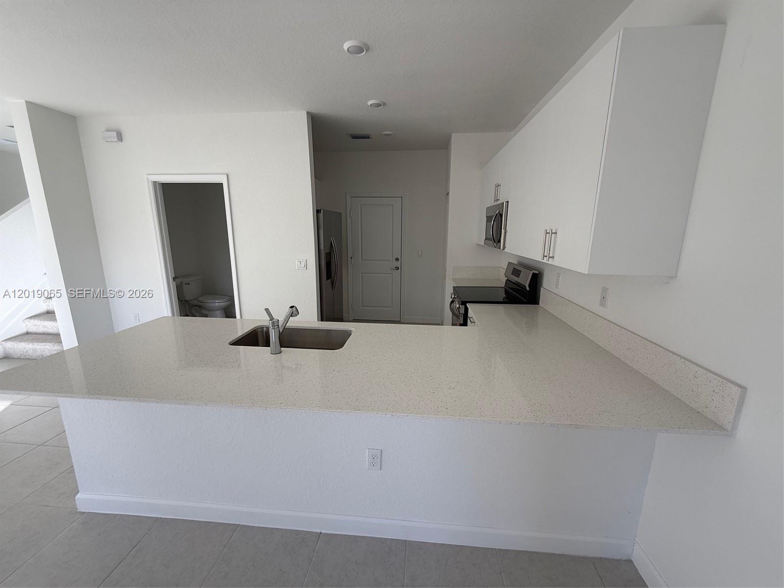 A kitchen features white cabinets, a quartz countertop island with a sink, and tile flooring — 4957 Oakmont Dr # 5838, Dania Beach FL 33312, DANIA BEACH, FL