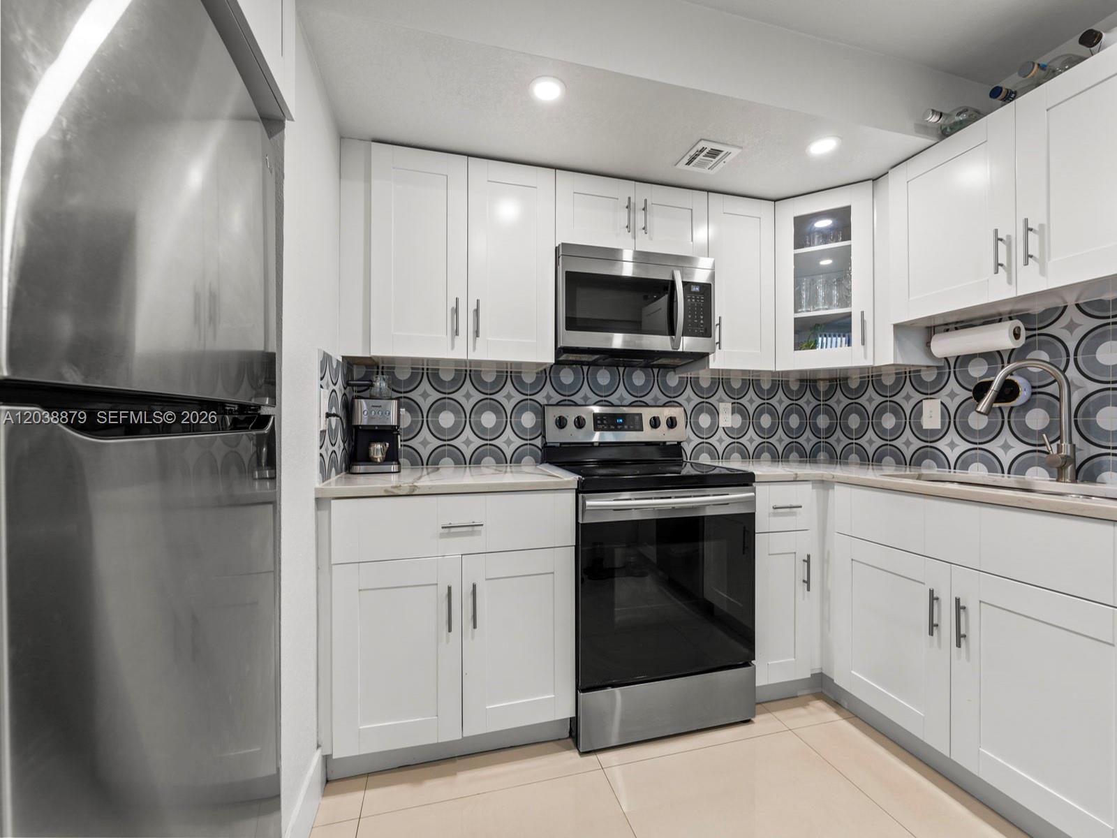 A kitchen features white cabinets, stainless steel appliances, and a patterned geometric tile backsplash — 7021 Environ Blvd # 320, Lauderhill FL 33319, LAUDERHILL, FL