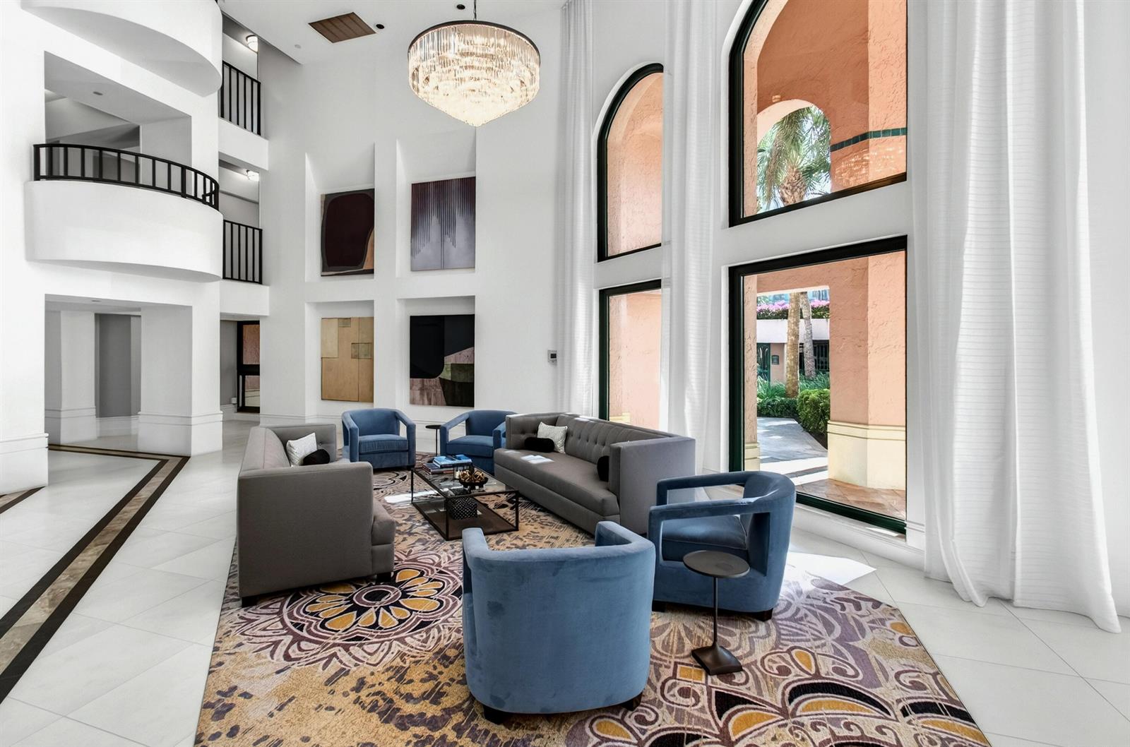 A spacious, high-ceilinged lobby features a seating area with blue armchairs and grey sofas — 140 SE 5th Avenue # 448, Boca Raton FL 33432, BOCA RATON, FL
