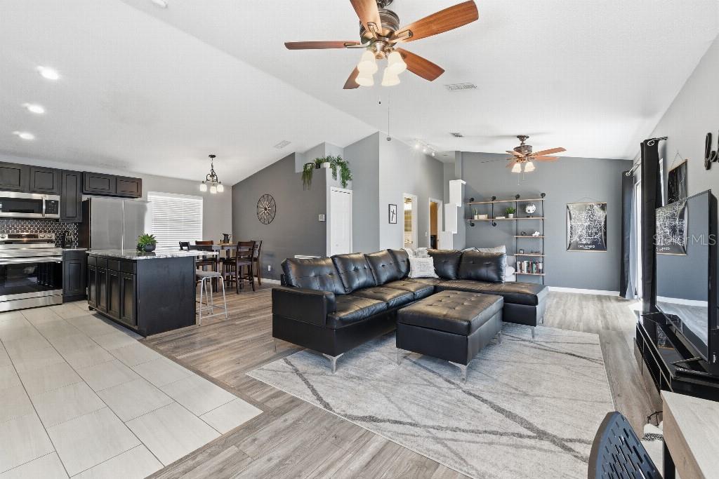 An open-concept living room and kitchen featuring dark cabinetry, a black sectional, and wood-look flooring — 25130 ENSLEY ROAD, SORRENTO, FL