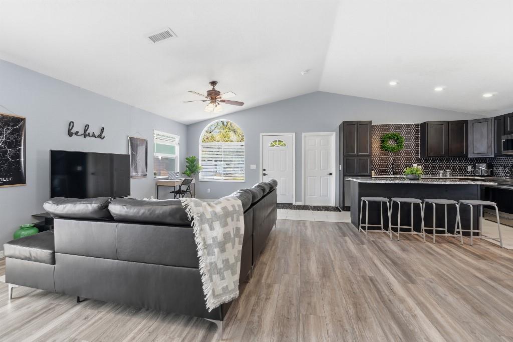 A living room with gray walls and wood-look flooring opens to a kitchen with dark cabinetry — 25130 ENSLEY ROAD, SORRENTO, FL
