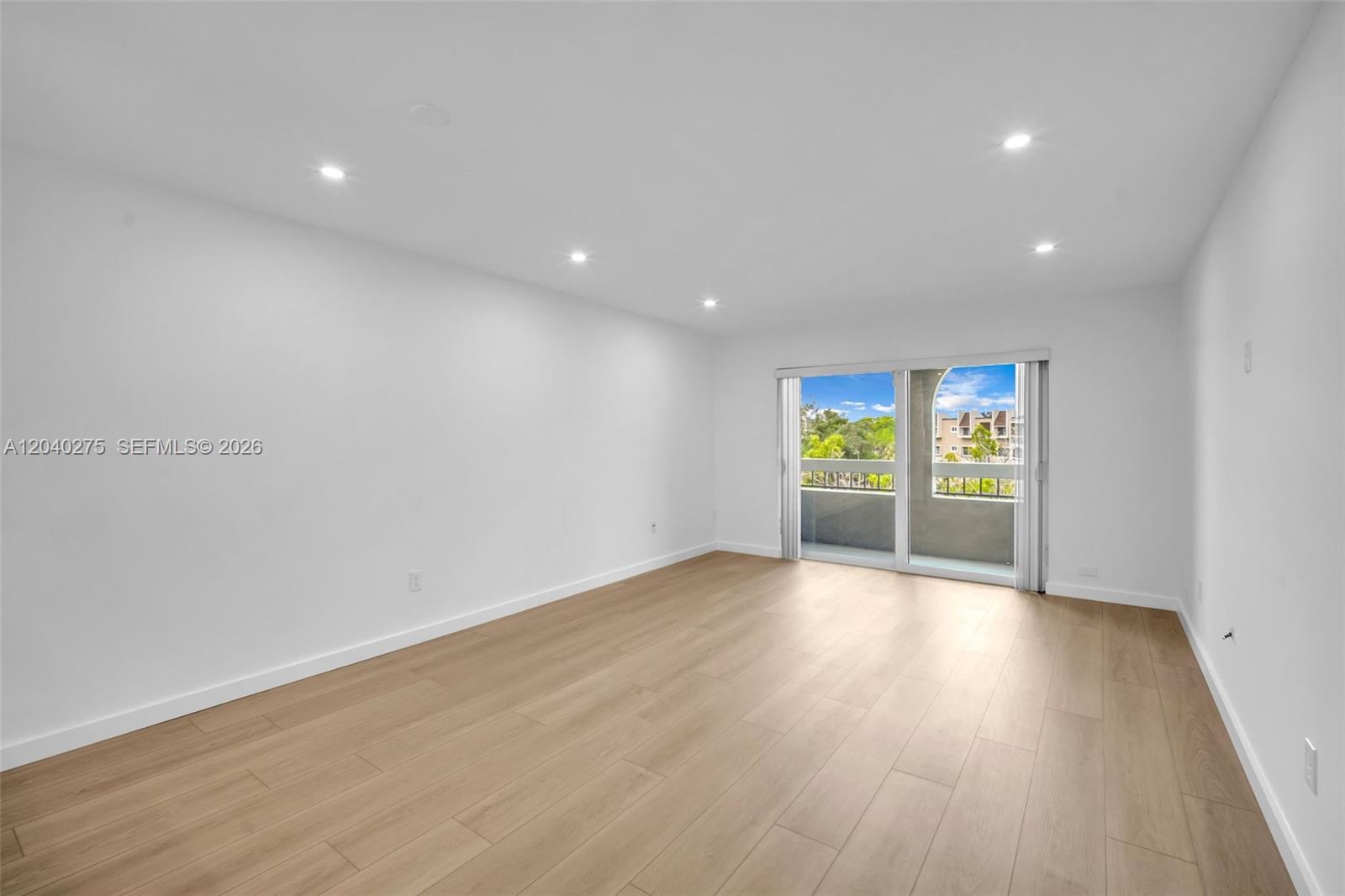 An empty room with white walls, light wood-look flooring, recessed lighting, and a sliding glass door — 8101 Camino Real # c402, Miami FL 33143, MIAMI, FL