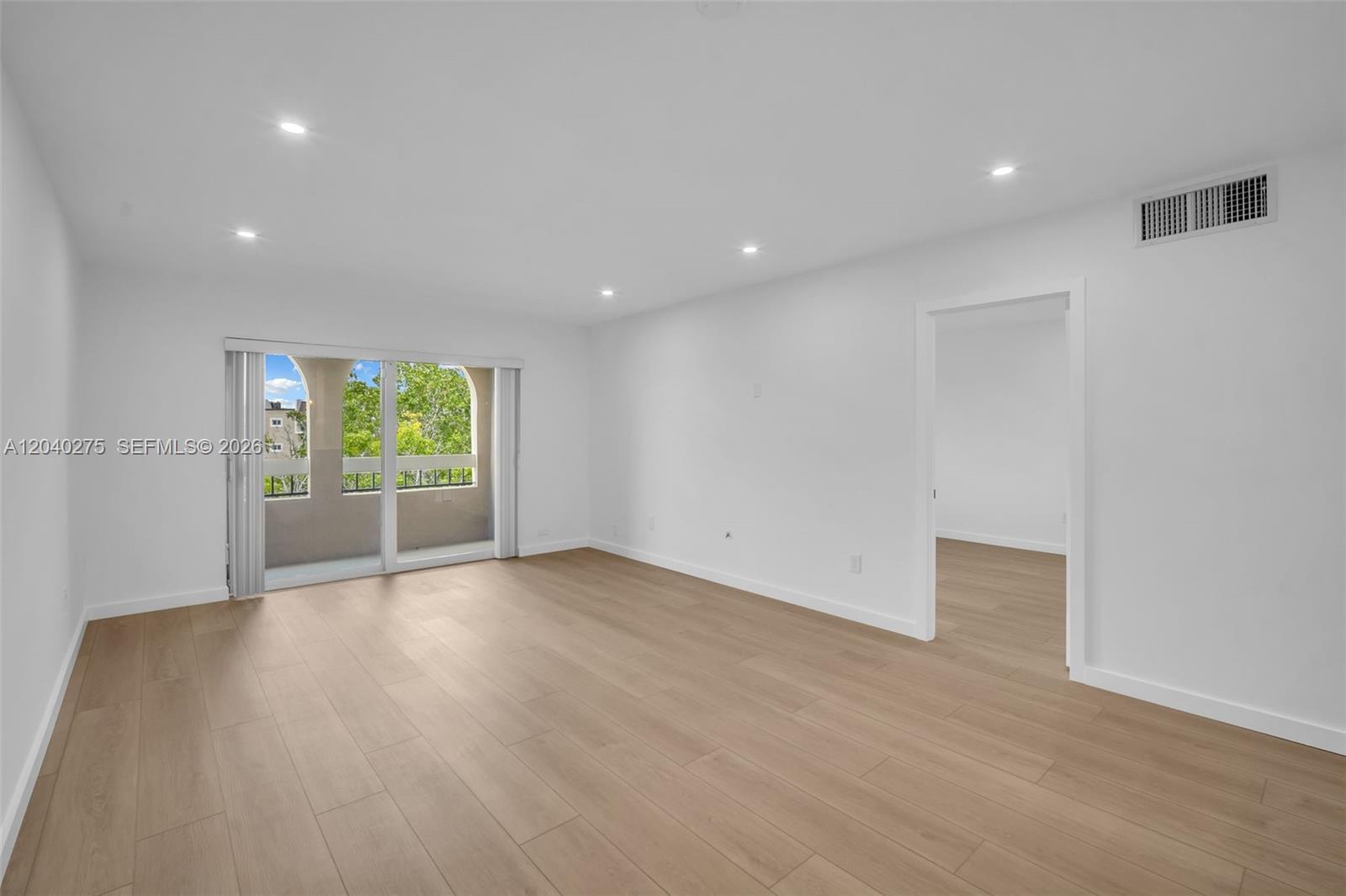A bright, empty room features light wood-look flooring, white walls, recessed lighting, and a balcony — 8101 Camino Real # c402, Miami FL 33143, MIAMI, FL