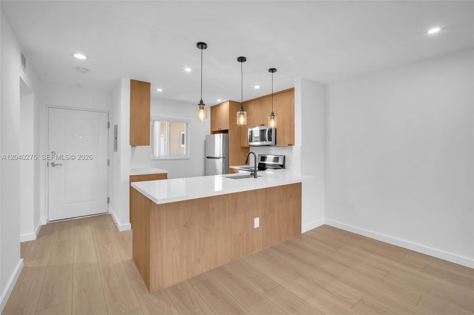 A kitchen features light wood cabinets, white countertops, a breakfast bar, and pendant lighting — 8101 Camino Real # c402, Miami FL 33143, MIAMI, FL