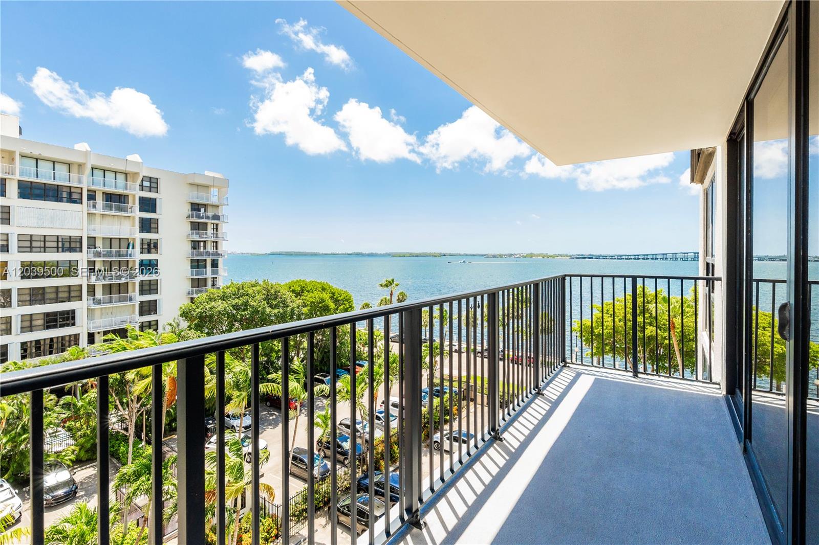 A balcony with a black metal railing overlooks a parking lot, trees, and the ocean — 1450 Brickell Bay Dr # 602, Miami FL 33131, MIAMI, FL