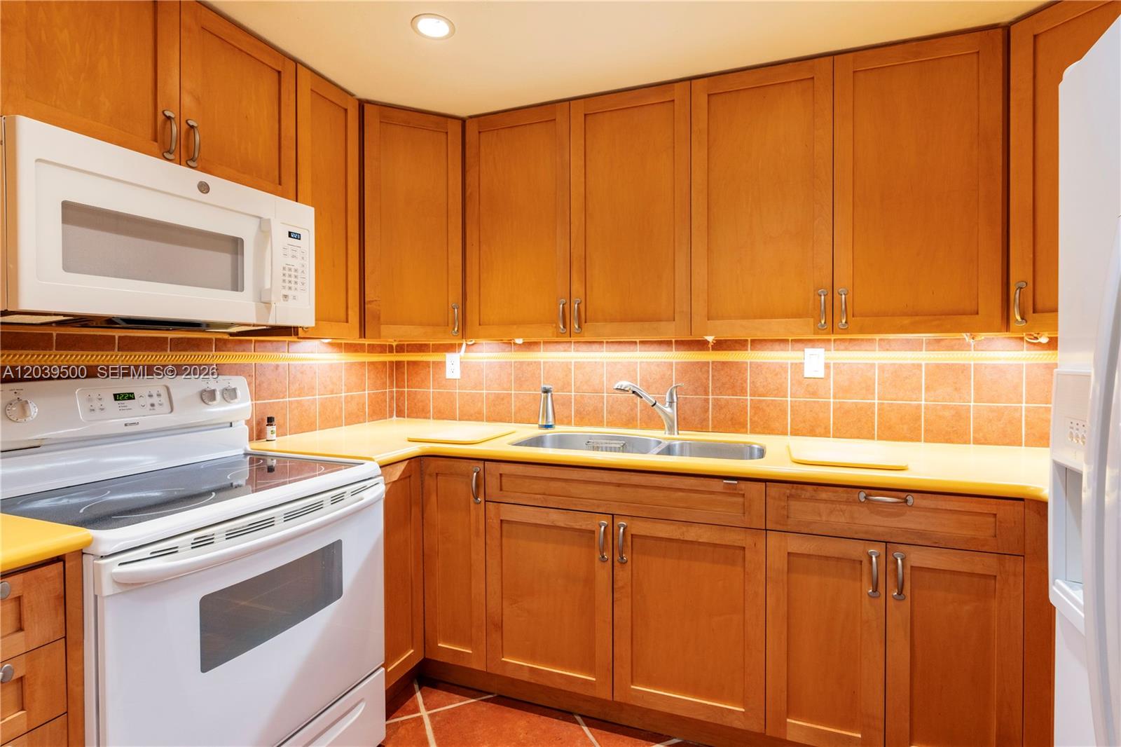 A kitchen features wood cabinets, yellow countertops, a white stove, and orange tiled walls — 1450 Brickell Bay Dr # 602, Miami FL 33131, MIAMI, FL
