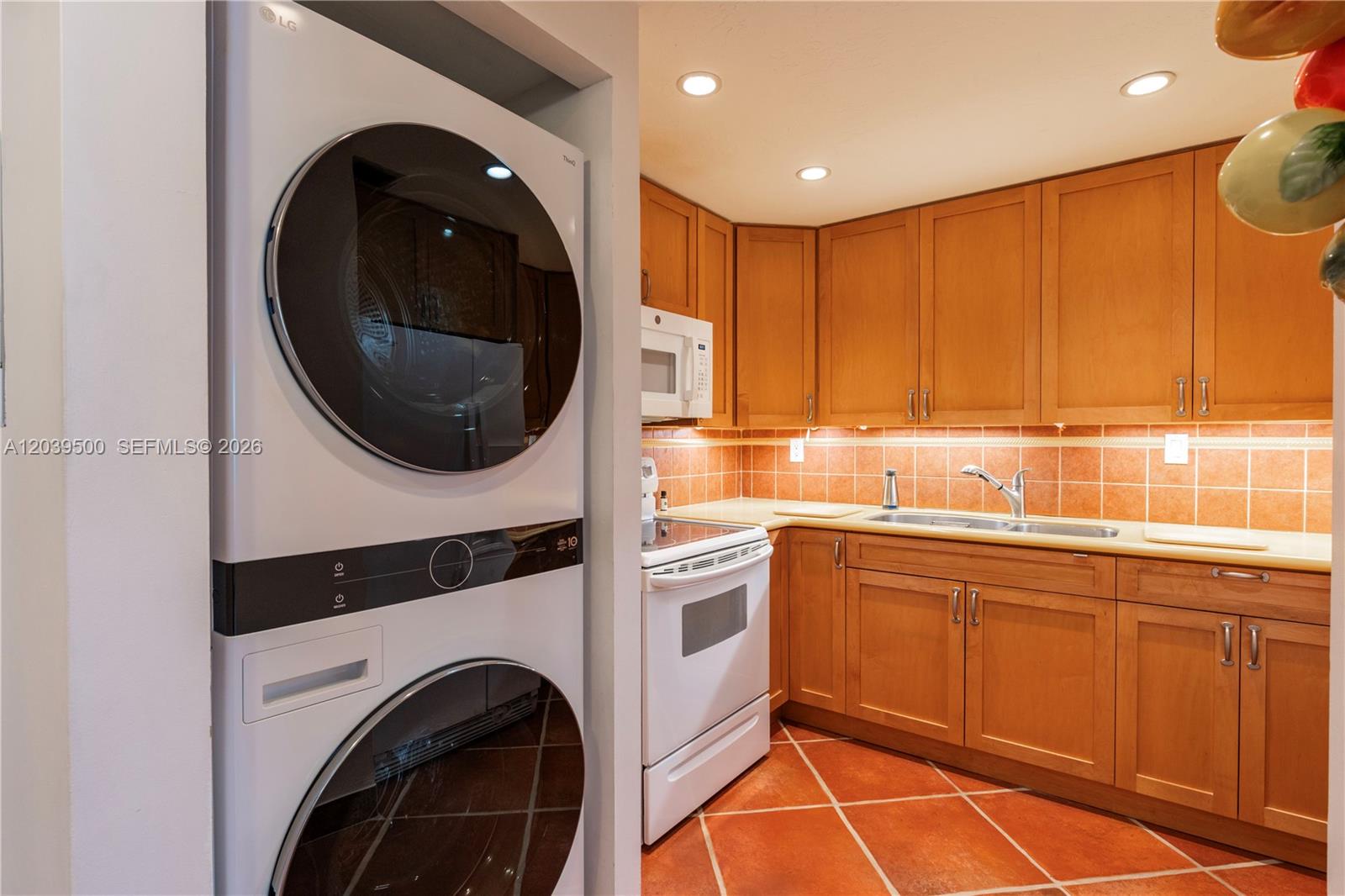 A kitchen features wooden cabinets, a tiled backsplash, and a stacked washer and dryer unit — 1450 Brickell Bay Dr # 602, Miami FL 33131, MIAMI, FL