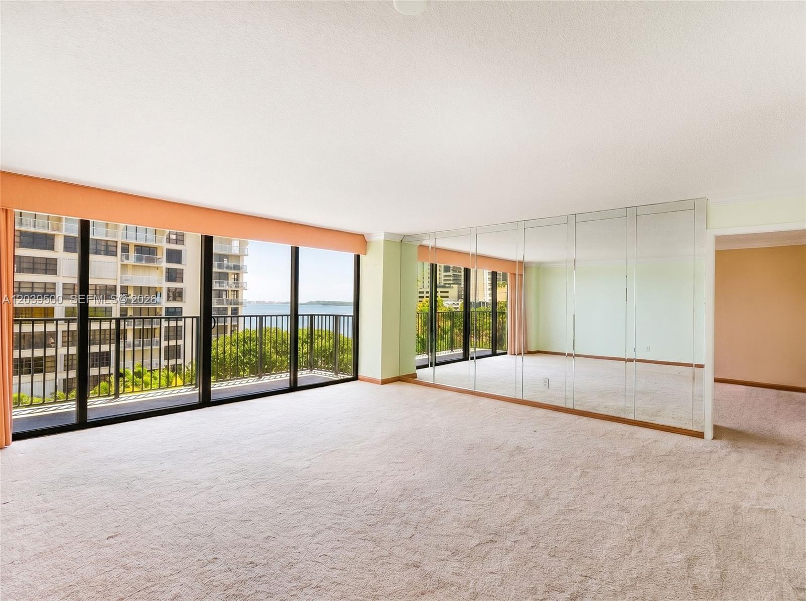 An empty room with beige carpeting, mirrored walls, and floor-to-ceiling windows overlooking the water — 1450 Brickell Bay Dr # 602, Miami FL 33131, MIAMI, FL