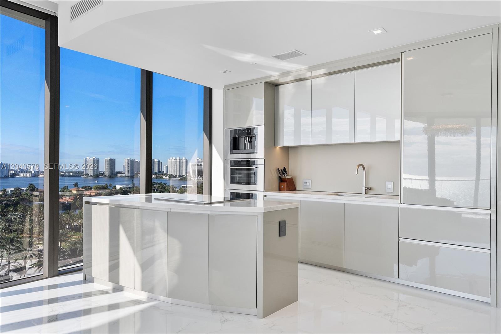 A modern kitchen features glossy light gray cabinets, a marble island, and floor-to-ceiling windows — 18975 Collins Ave # 2004, Sunny Isles Beach FL 33160, SUNNY ISLES BEACH, FL