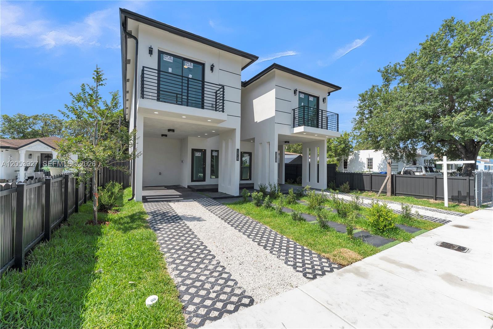 A modern two-story duplex features white stucco exteriors, black railings, and paved gravel driveways — 1818 NW 49th St, Miami FL 33142, MIAMI, FL