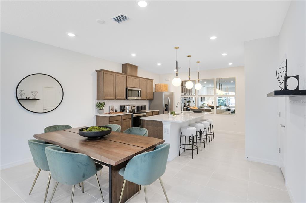 A modern kitchen and dining area features wood cabinets, a white island, and teal chairs — 11446 NONA SOUND STREET, ORLANDO, FL