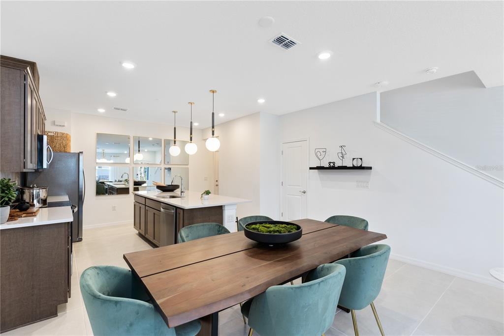 A dining area with a wooden table and teal chairs sits adjacent to a modern kitchen — 11446 NONA SOUND STREET, ORLANDO, FL