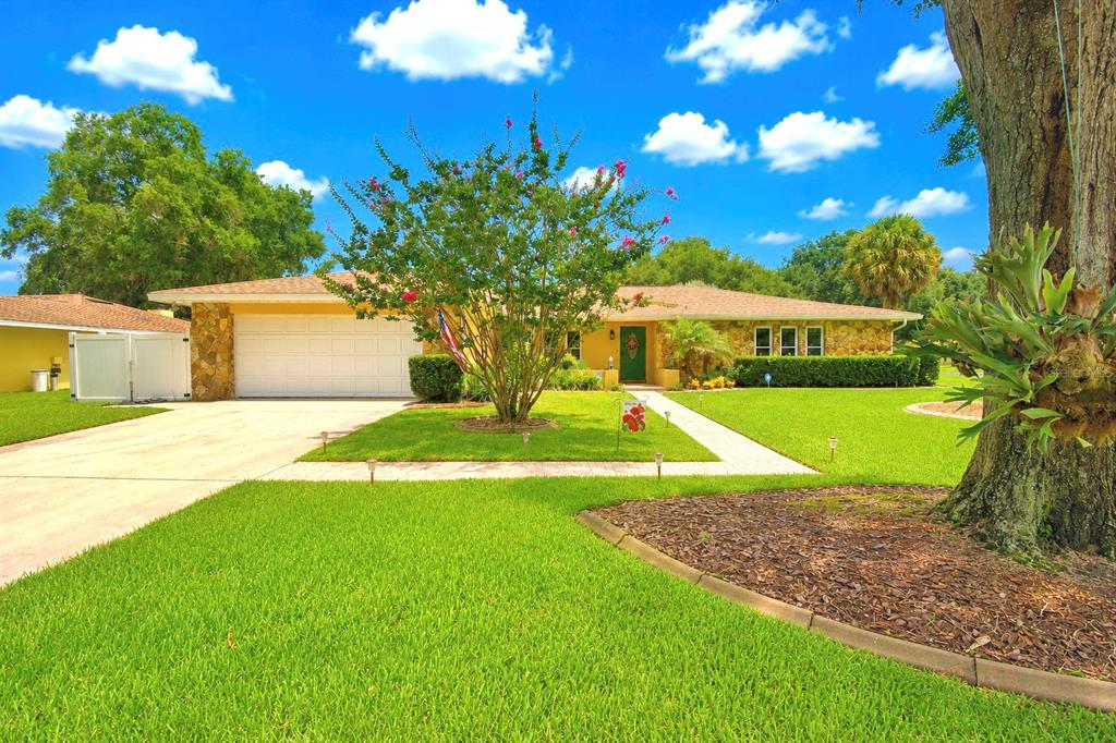 A single-story house with a white garage, stone accents, and a large tree in front — 902 CRESTVIEW DRIVE, AUBURNDALE, FL