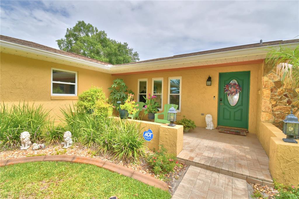 A yellow house exterior features a green front door, a stone accent wall, and landscaping — 902 CRESTVIEW DRIVE, AUBURNDALE, FL