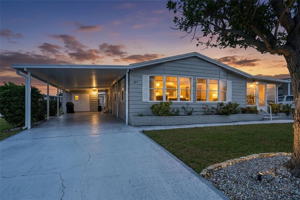 A single-story house with gray siding, a carport, and a front lawn at sunset — 487 LOMA LINDA, NORTH PORT, FL