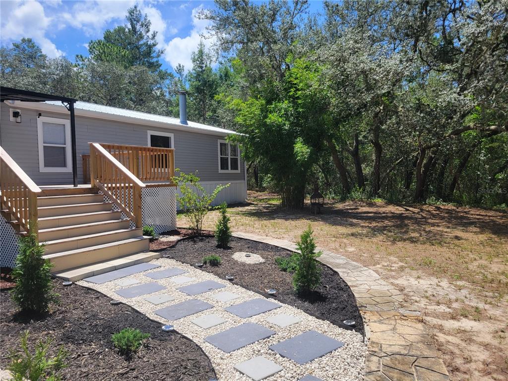 A gray mobile home features a wooden deck with stairs and a stone walkway — 7597 N BRUTUS AVENUE, DUNNELLON, FL