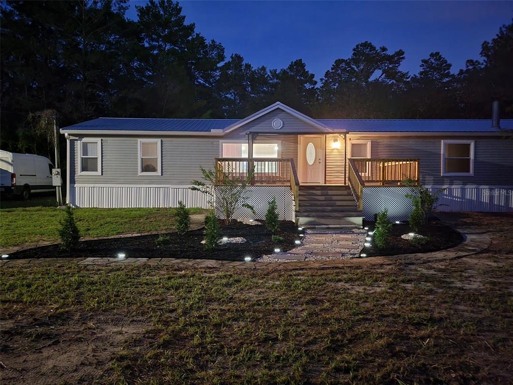 A single-story house with a metal roof, wooden deck, and landscaped front yard at dusk — 7597 N BRUTUS AVENUE, DUNNELLON, FL
