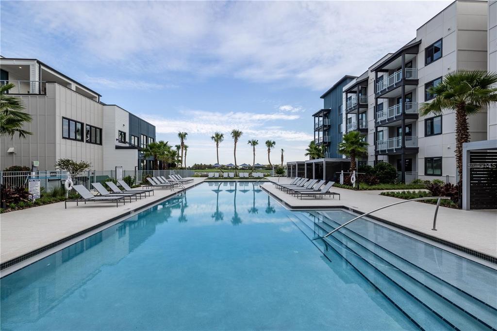 A rectangular swimming pool is centered between two modern apartment buildings with lounge chairs — 5127 W TYSON AVENUE UNIT TH1, TAMPA, FL