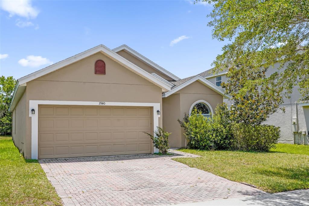 A tan single-story house with a two-car garage and a brick paver driveway — 3940 HEATHCOTE DRIVE, ORLANDO, FL