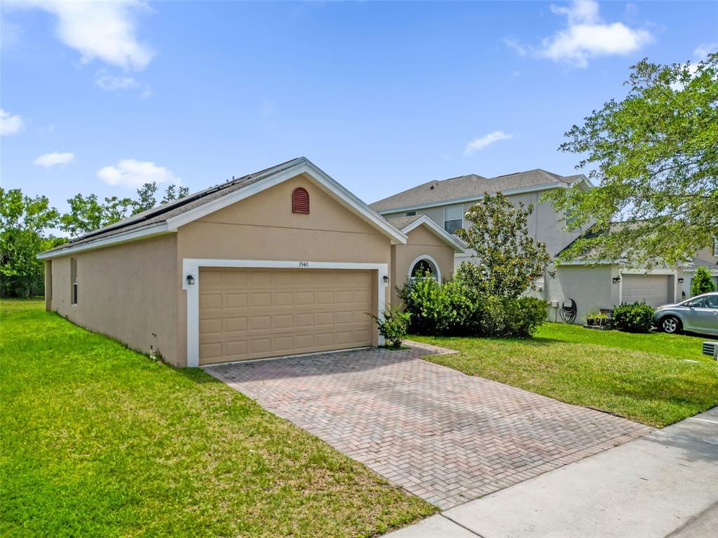 A tan single-story house with a two-car garage and a brick paver driveway — 3940 HEATHCOTE DRIVE, ORLANDO, FL