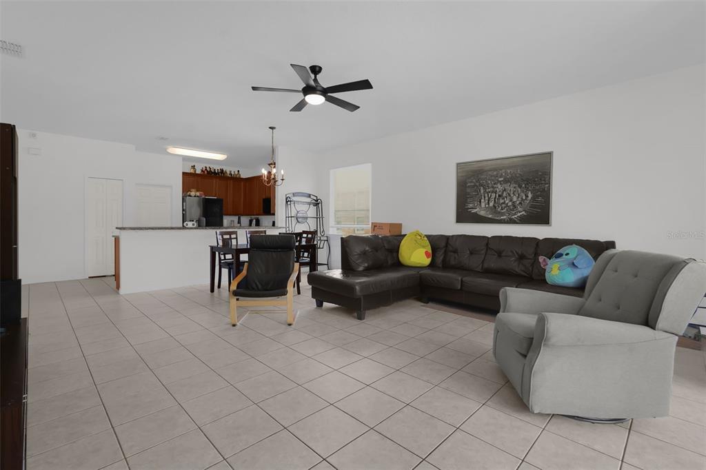 An open-concept living and dining area features tile flooring, a dark sectional, and kitchen cabinetry — 3940 HEATHCOTE DRIVE, ORLANDO, FL