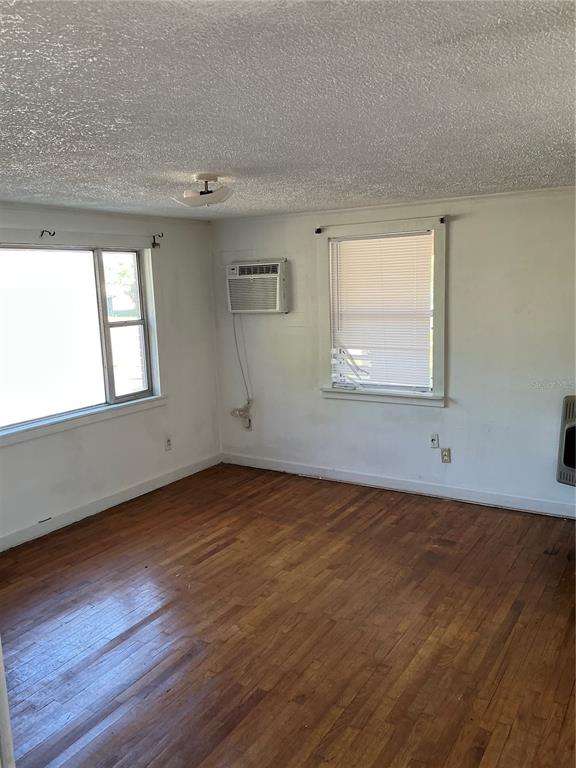 An empty room features hardwood floors, white walls, two windows, and a wall-mounted air conditioner — 2893 EVA MAE STREET, MARIANNA, FL