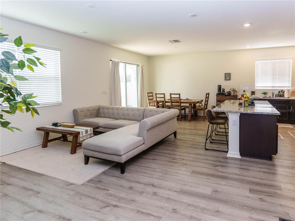 An open-concept living and dining area features a sectional sofa, kitchen island, and wood flooring — 37501 WILLIAMETTE WAY, ZEPHYRHILLS, FL
