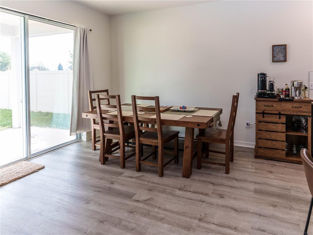A dining room features a wooden table and chairs, light wood-look flooring, and a sliding door — 37501 WILLIAMETTE WAY, ZEPHYRHILLS, FL