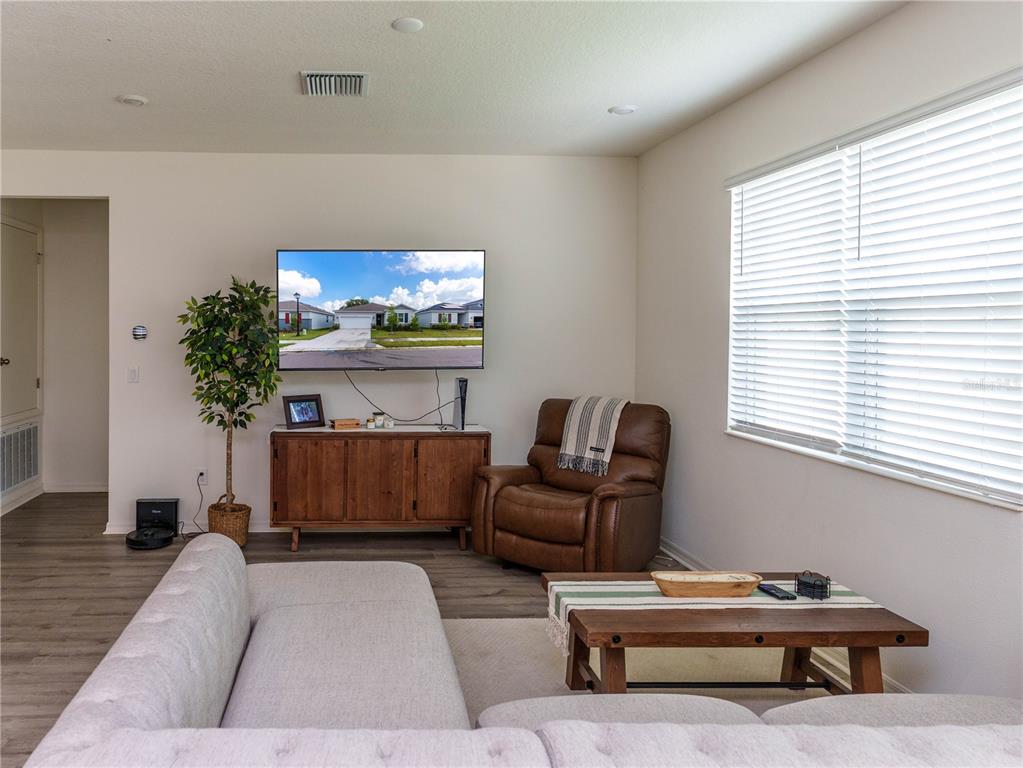 A living room features a wall-mounted television, a wooden console, a leather recliner, and sectional seating — 37501 WILLIAMETTE WAY, ZEPHYRHILLS, FL
