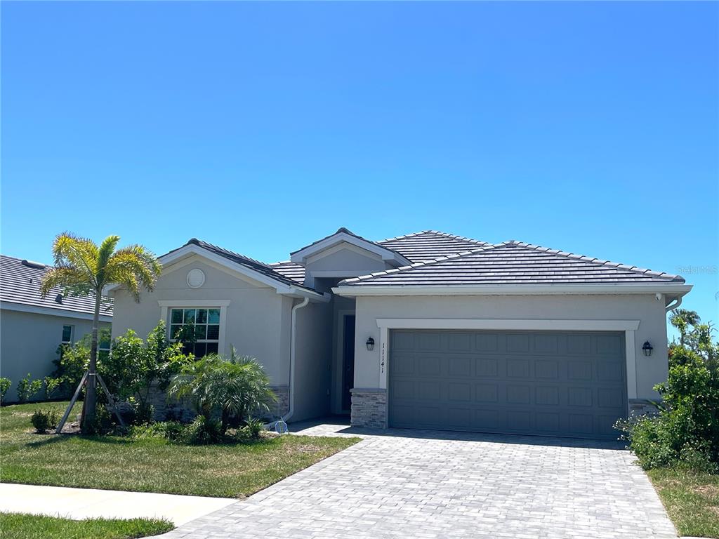 A single-story house with a gray garage, stone accents, and a paved driveway under blue sky — 11141 PINOT DRIVE, VENICE, FL