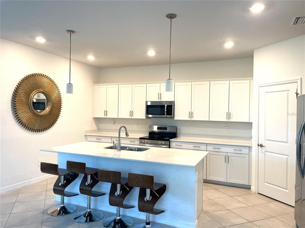 A kitchen features white cabinets, a central island with bar stools, and stainless steel appliances — 11141 PINOT DRIVE, VENICE, FL