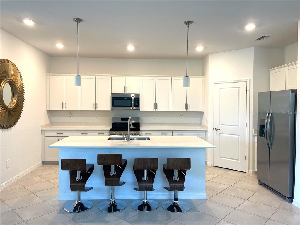A modern kitchen features white cabinets, a central island with four barstools, and stainless appliances — 11141 PINOT DRIVE, VENICE, FL