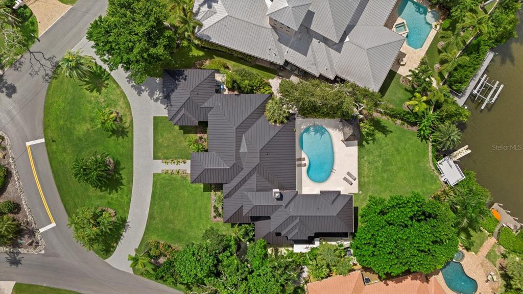 An aerial view shows a house with a dark metal roof, pool, and landscaped yard — 1707 CARIBBEAN DRIVE, SARASOTA, FL