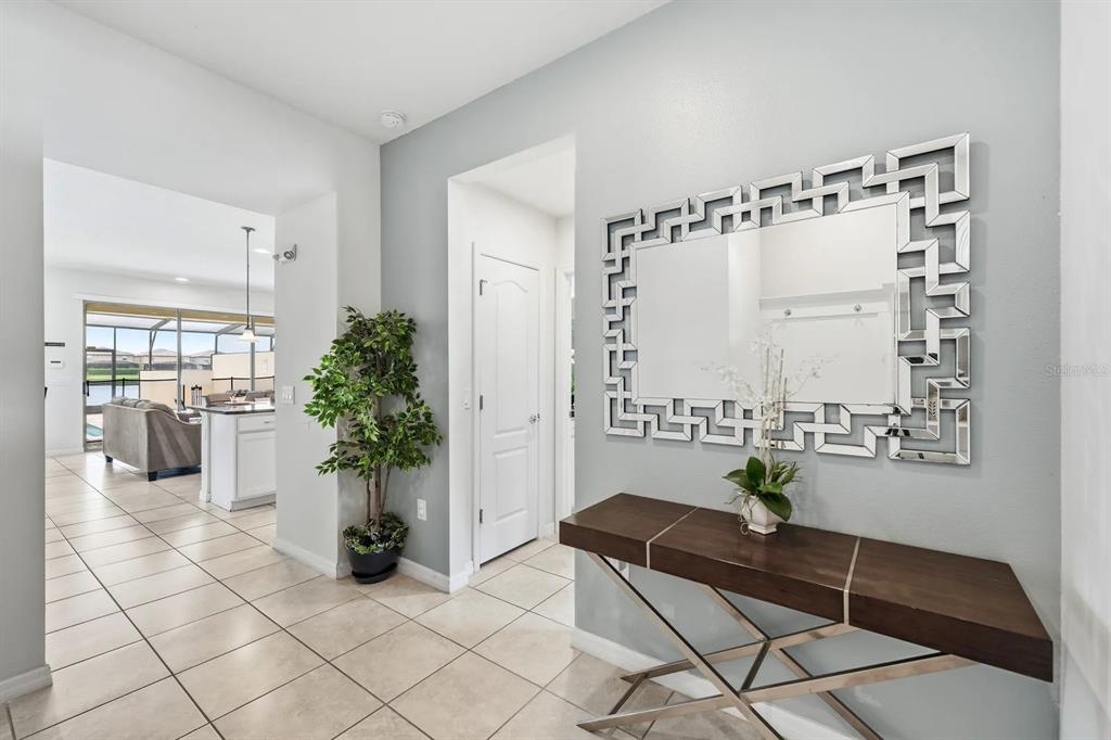 A tiled entryway features a console table, a decorative mirror, and a view into the kitchen — 8866 GENEVE COURT, KISSIMMEE, FL