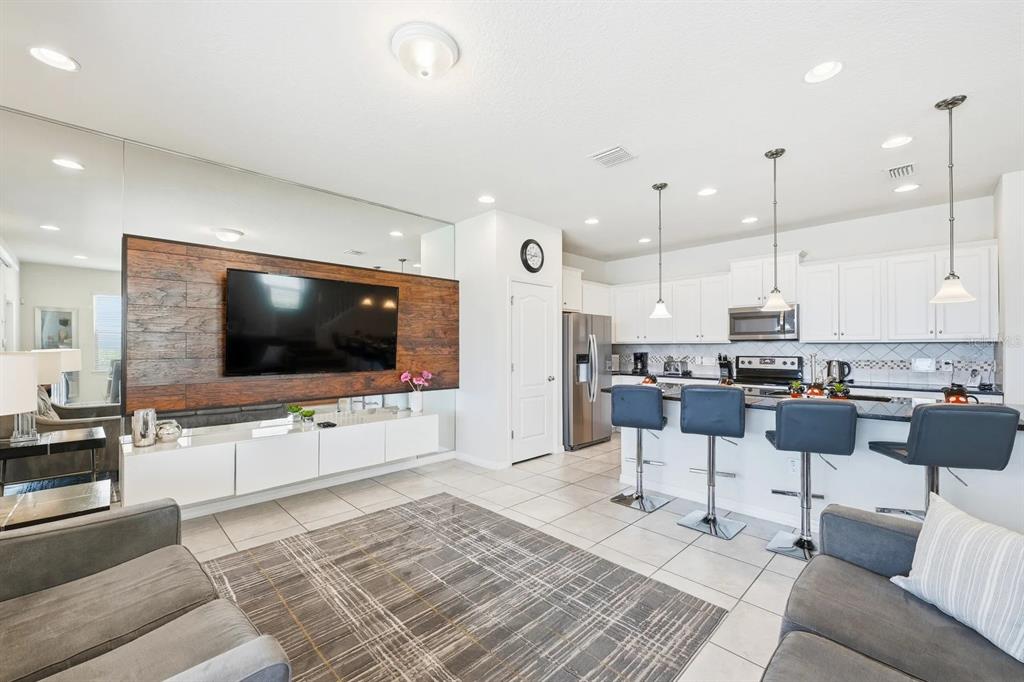 A living room with a wood-paneled TV wall and an open kitchen with bar seating — 8866 GENEVE COURT, KISSIMMEE, FL