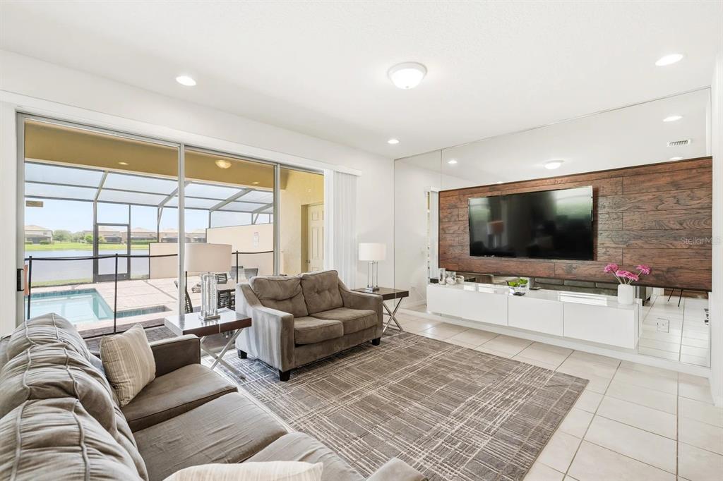 A living room features a wood-paneled accent wall, a floating media console, and sliding glass doors — 8866 GENEVE COURT, KISSIMMEE, FL