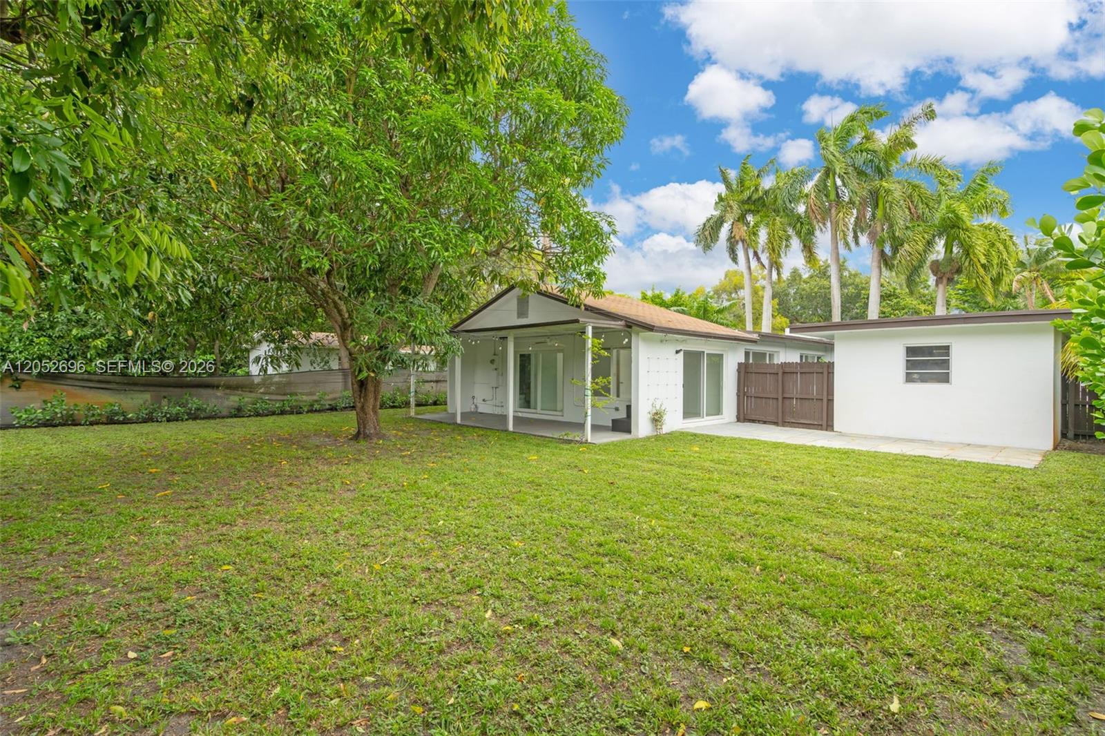A white house with a covered patio and a large backyard featuring a mature tree — 1580 NE 139th St, North Miami FL 33161, NORTH MIAMI, FL