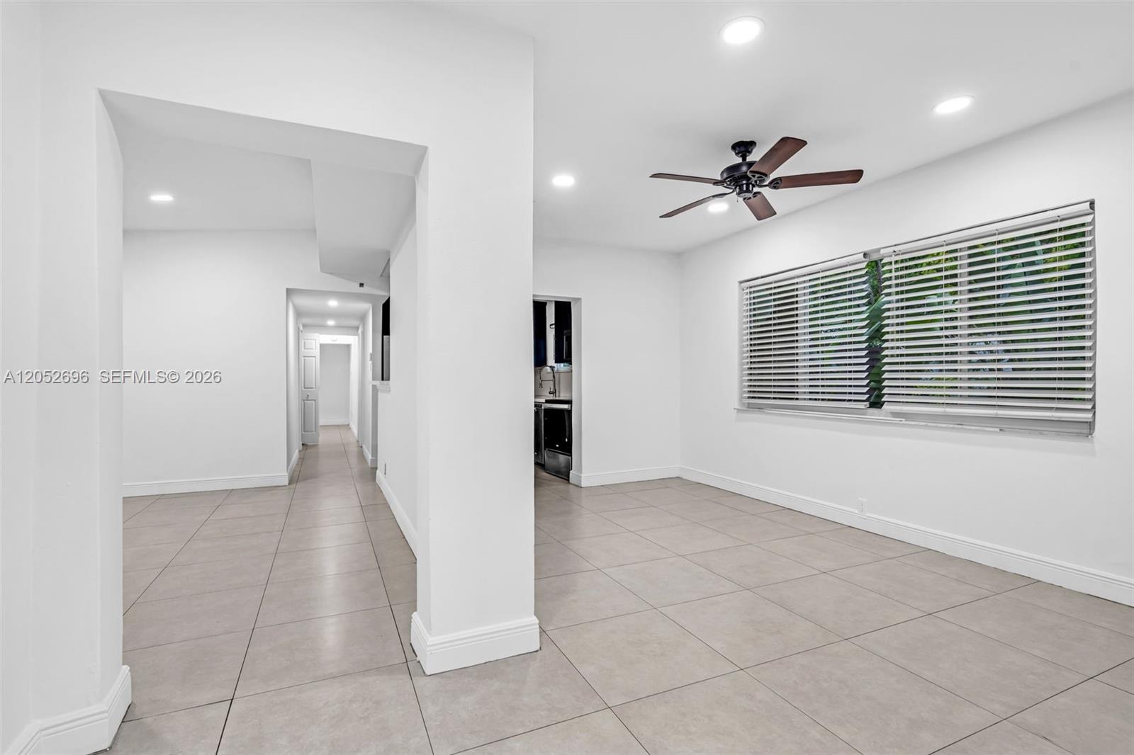 A bright, empty room features white walls, large light-colored floor tiles, and a ceiling fan — 1580 NE 139th St, North Miami FL 33161, NORTH MIAMI, FL