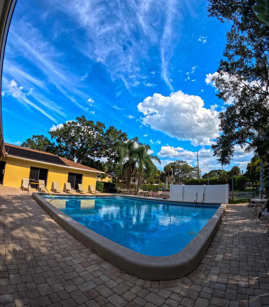 A rectangular swimming pool sits on a brick patio next to a yellow building — 400 18th Street # D, Vero Beach FL 32960, VERO BEACH, FL